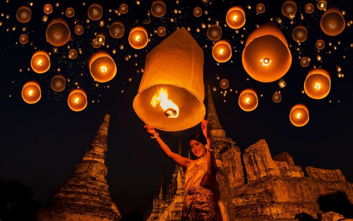 A woman holding a floating lamp with fire set inside at night time to symbolize an important event