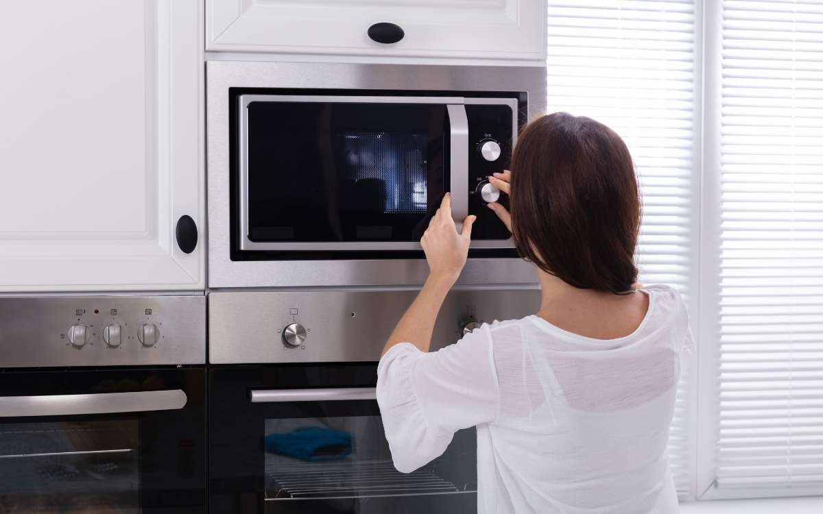 A woman turning the knob of a microwave oven placed in a cabinet_Can You Put a Microwave in a Cabinet