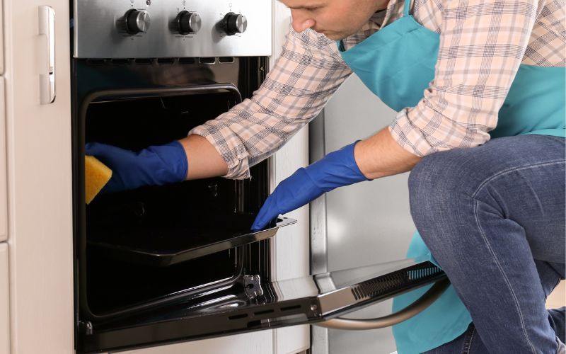 A man wearing gloves and cleaning the inside of oven