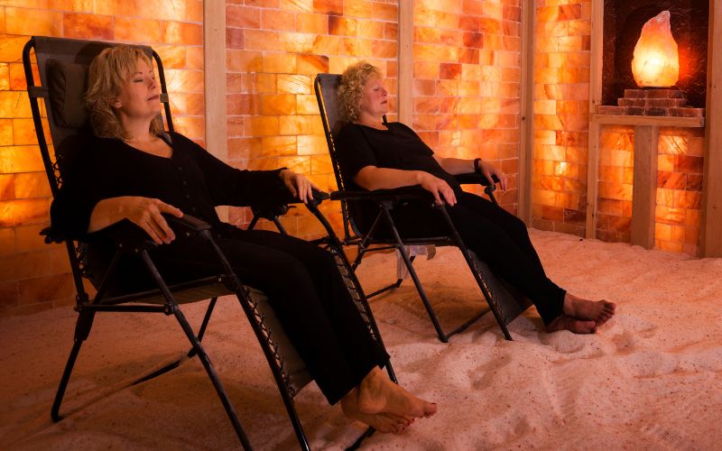 two women sitting on a chair in a room with pink Himalayan salts with salt lamp
