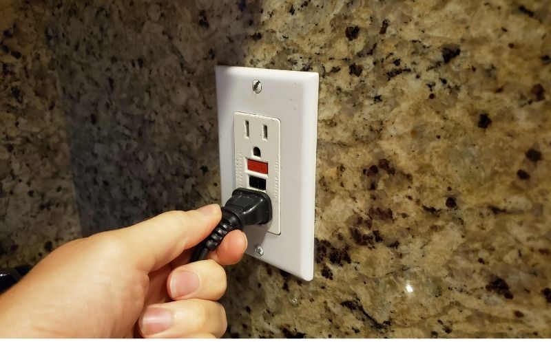 A hand holding a plug still attached in outlet