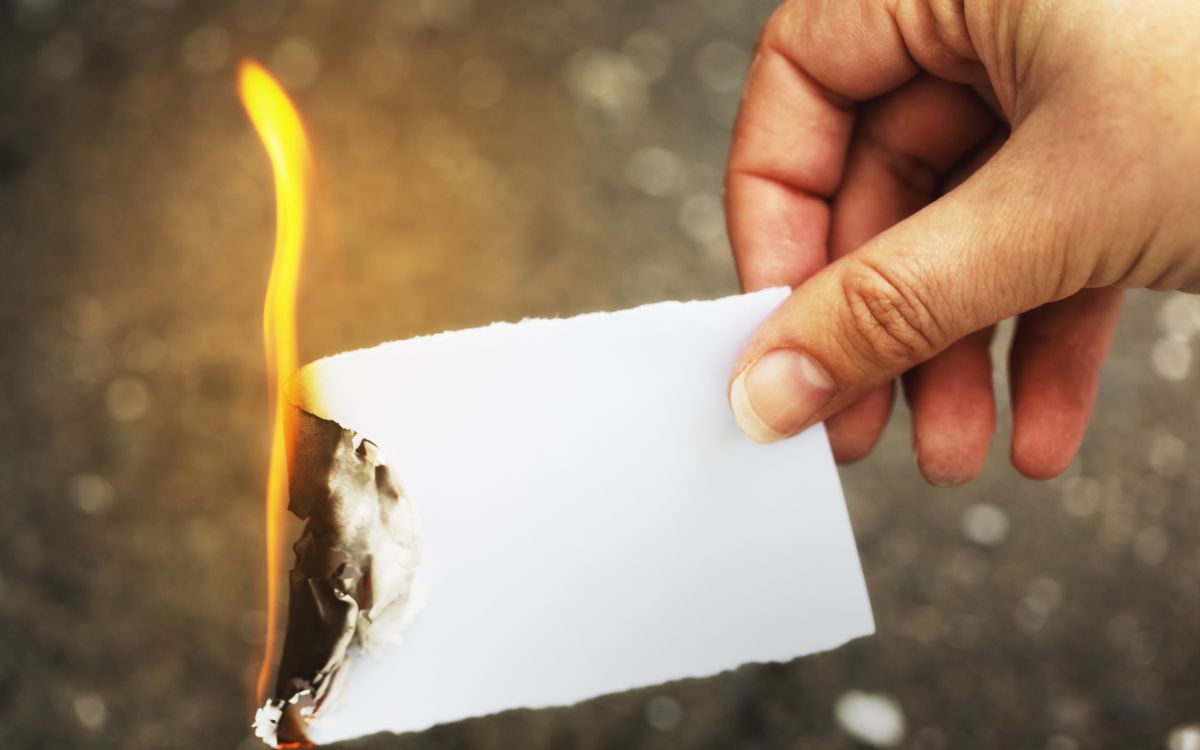 Hand holding a burning piece of paper_What Temperature Does Paper Burn Featured Image